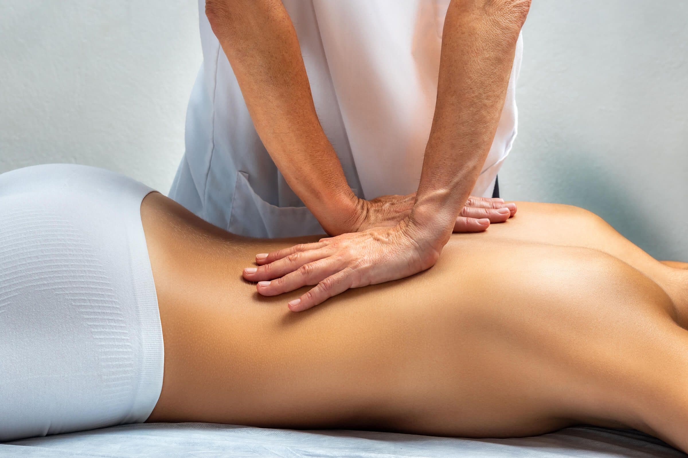 Manuelle Therapie: Behandlung des Rückens mit beiden Händen bei PhysiOsMedix